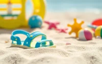 Kindersandalen im Sand, umgeben von bunten Spielsachen am Strand